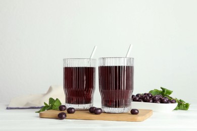 Delicious acai juice in glasses, berries and mint on white wooden table