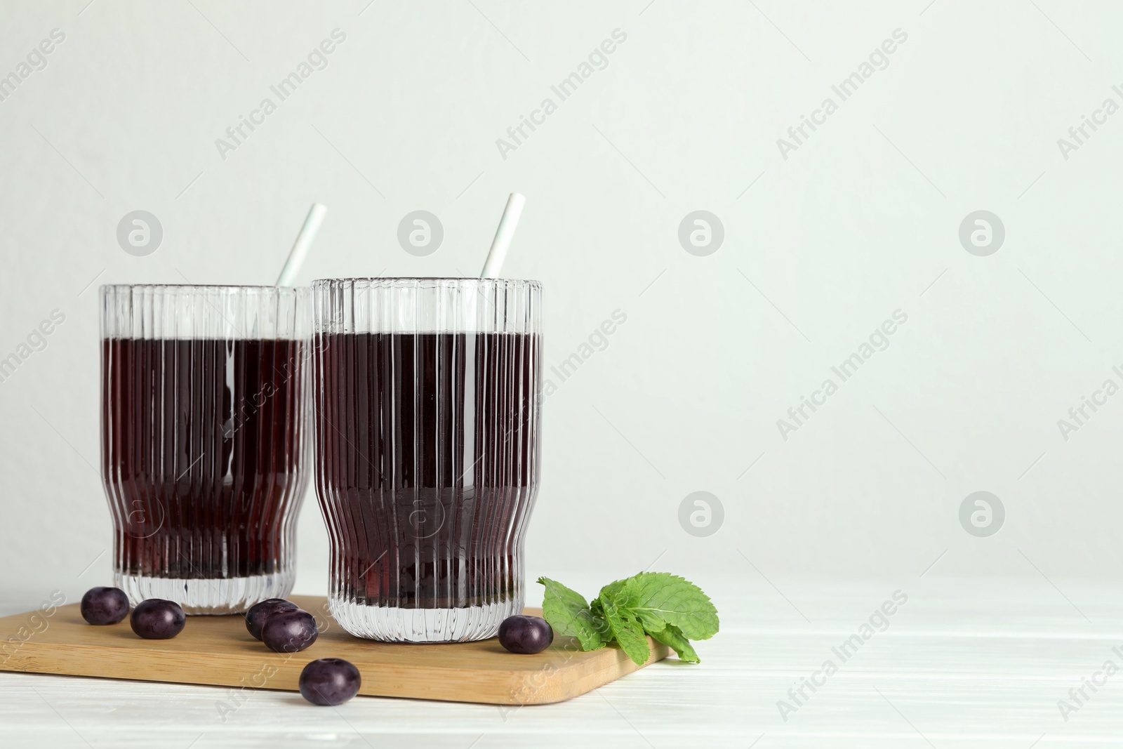 Photo of Delicious acai juice in glasses, berries and mint on white wooden table. Space for text