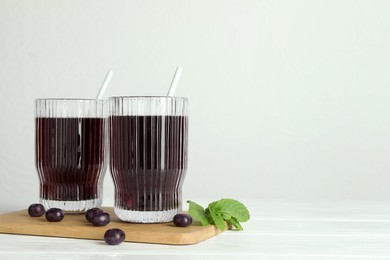 Photo of Delicious acai juice in glasses, berries and mint on white wooden table. Space for text