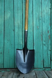 Photo of Metal shovel near turquoise wooden wall. Gardening tool