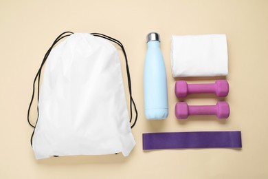 Photo of White drawstring bag and sports equipment on beige background, flat lay