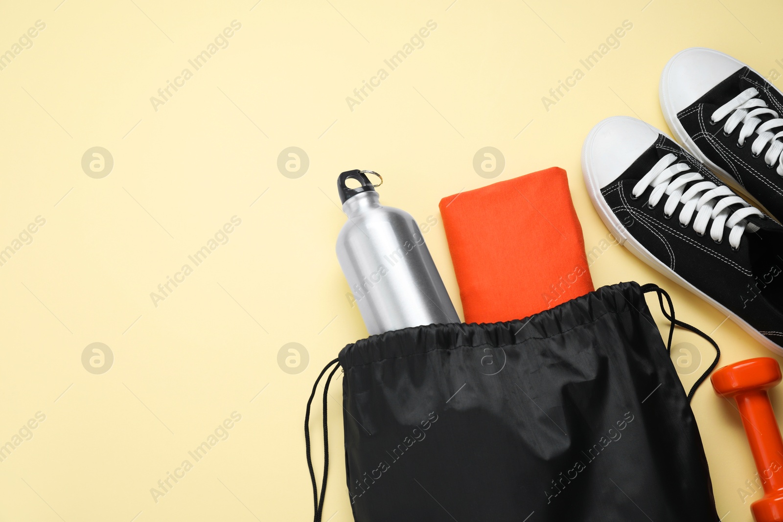 Photo of Black drawstring bag, sneakers, thermo bottle and cloth on beige background, flat lay. Space for text