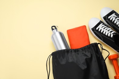 Photo of Black drawstring bag, sneakers, thermo bottle and cloth on beige background, flat lay. Space for text