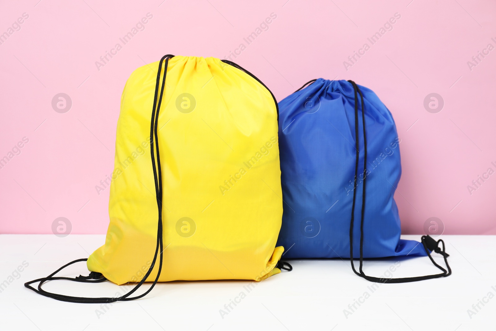 Photo of Two drawstring bags on white wooden table against pink background