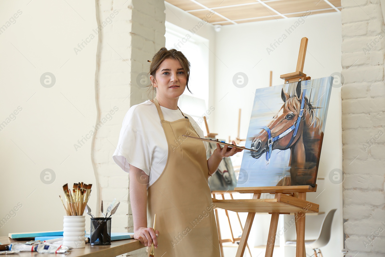 Photo of Woman with brush and palette near easel in drawing studio