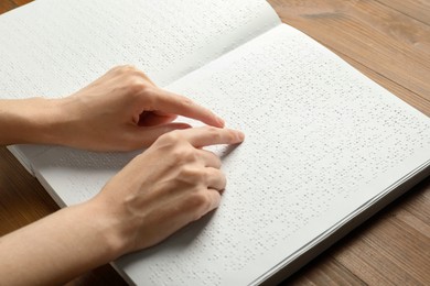 Blind woman reading book written in Braille at wooden table, closeup