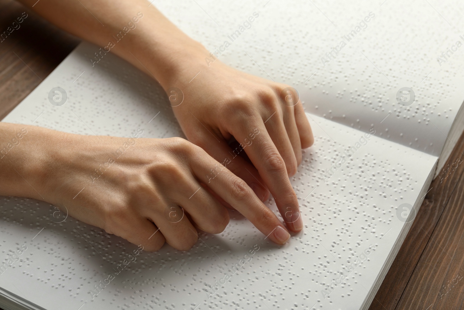 Photo of Blind woman reading book written in Braille at wooden table, closeup