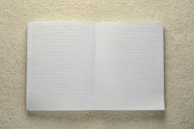 Photo of Book with Braille text on beige textured table, top view. Education and leisure for blind people