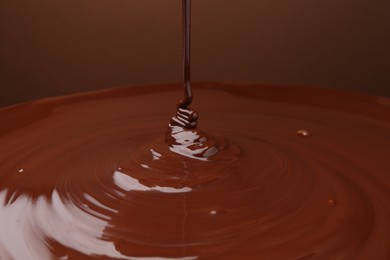 Photo of Pouring delicious melted chocolate on brown background, closeup