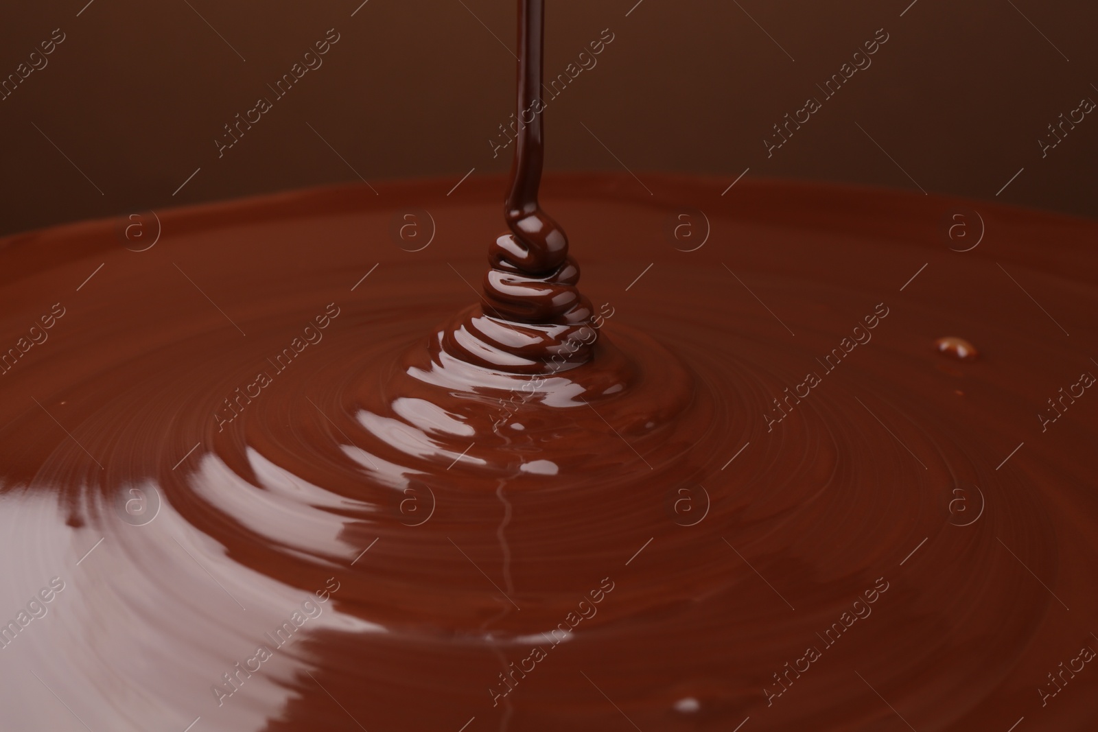 Photo of Pouring delicious melted chocolate on brown background, closeup