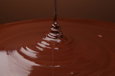 Photo of Pouring delicious melted chocolate on brown background, closeup