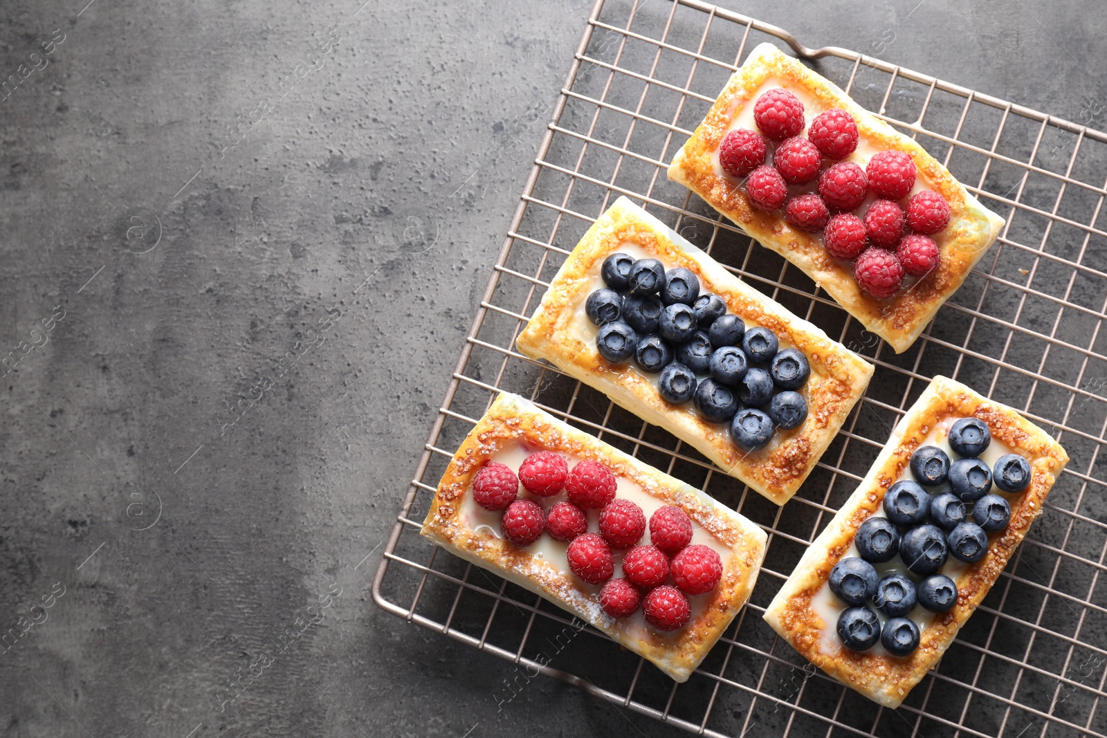 Photo of Tasty puff pastries with berries on grey table, top view. Space for text