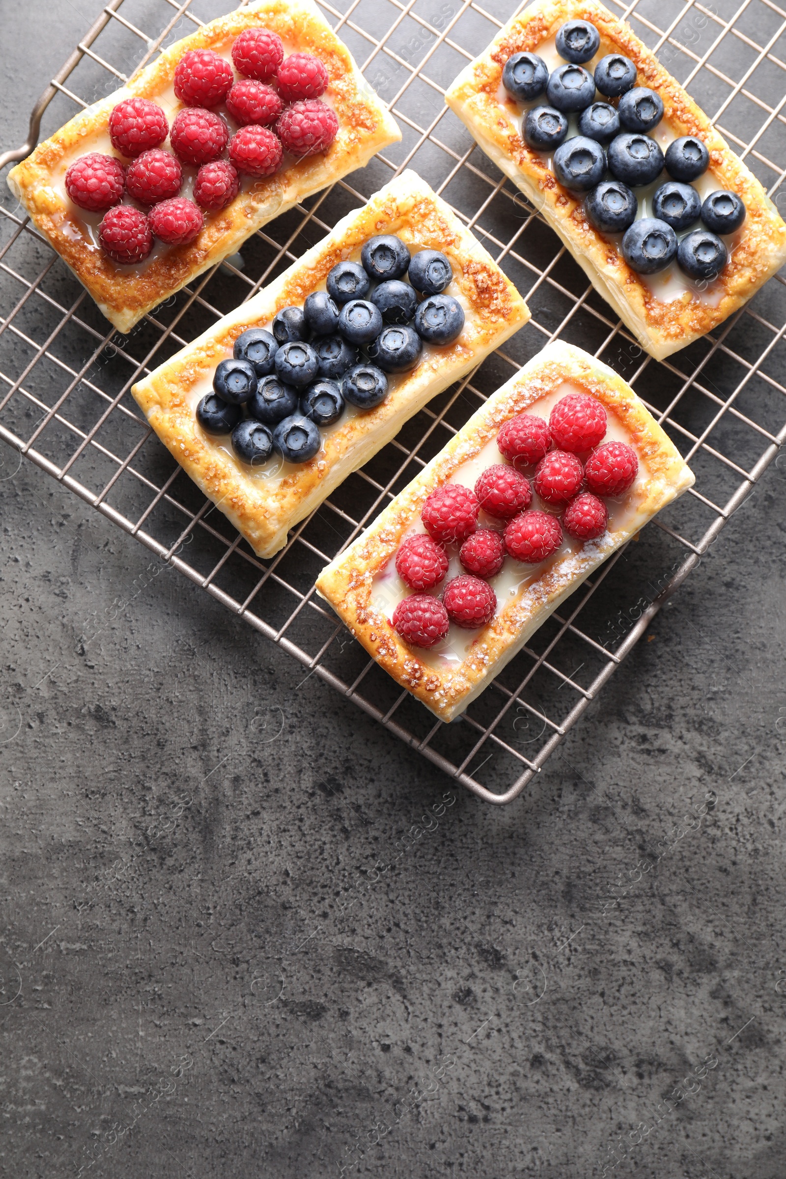 Photo of Tasty puff pastries with berries on grey table, top view. Space for text