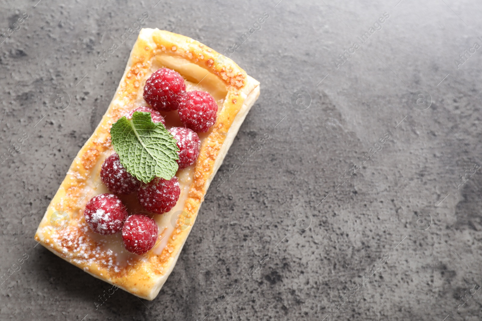 Photo of Tasty puff pastry with raspberries and mint on grey table, top view. Space for text