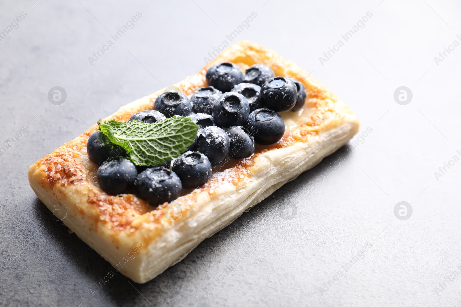 Photo of Tasty puff pastry with blueberries and mint on grey table, closeup. Space for text