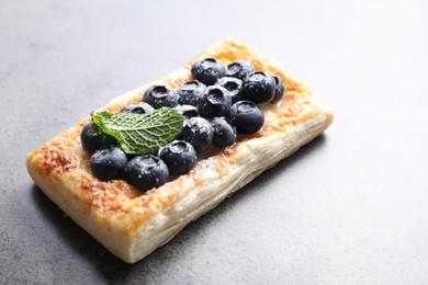 Photo of Tasty puff pastry with blueberries and mint on grey table, closeup. Space for text