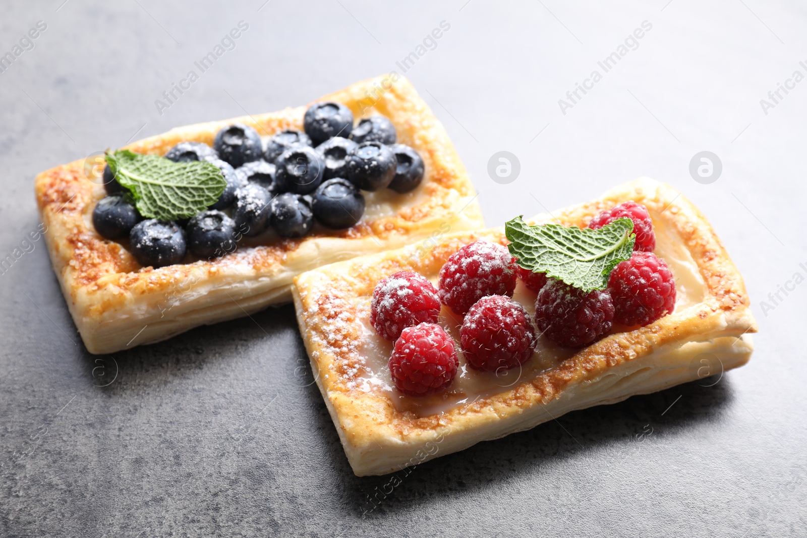 Photo of Tasty puff pastries with berries on grey table