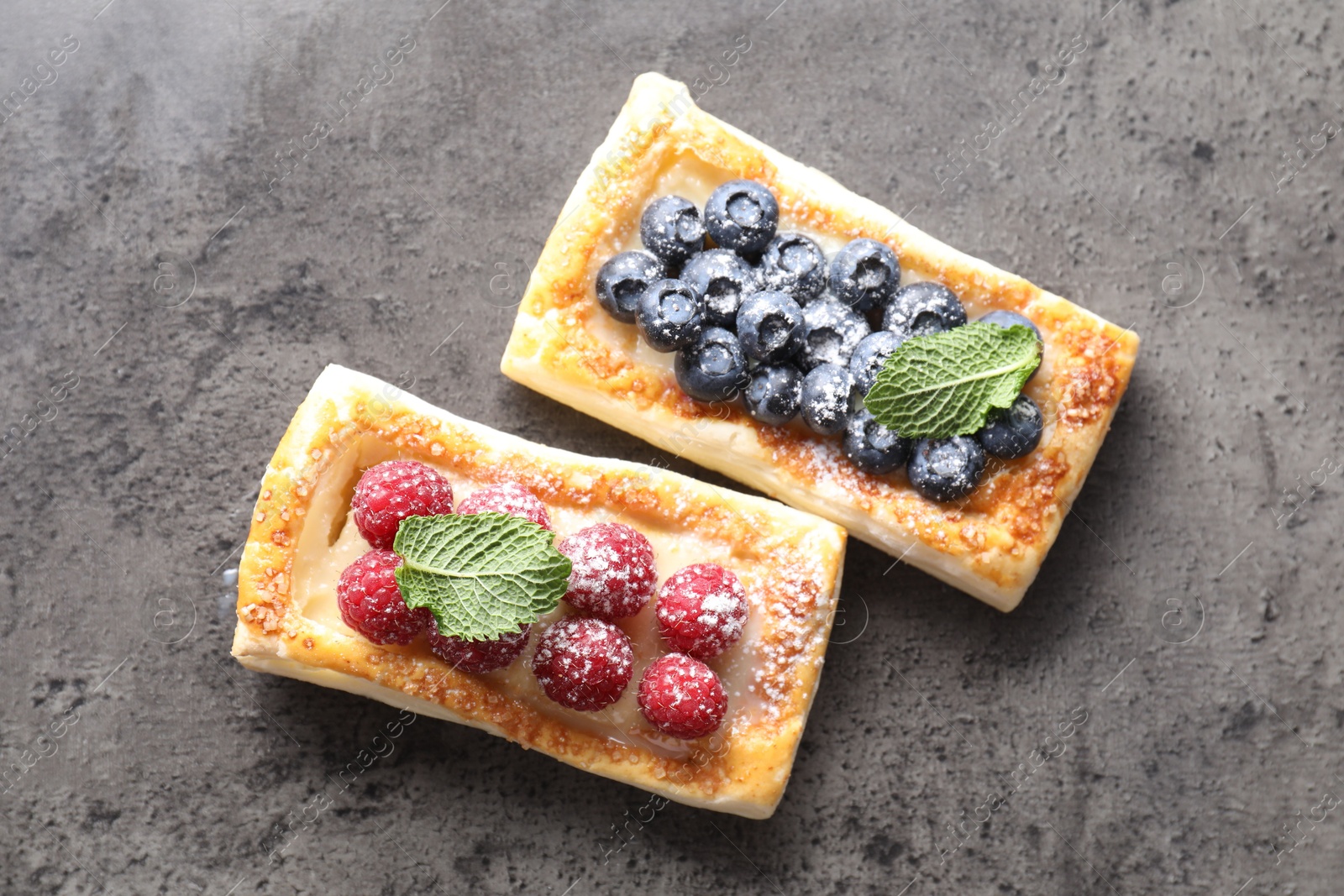 Photo of Tasty puff pastries with berries and powdered sugar on grey table, flat lay