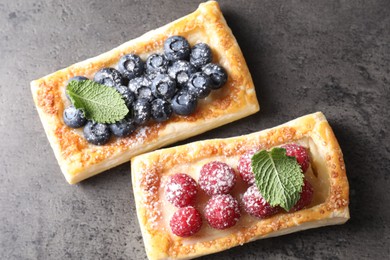 Tasty puff pastries with berries and powdered sugar on grey table, flat lay