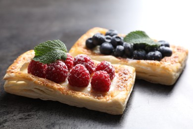 Tasty puff pastries with berries on grey table, closeup