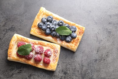 Tasty puff pastries with berries and powdered sugar on grey table, flat lay. Space for text