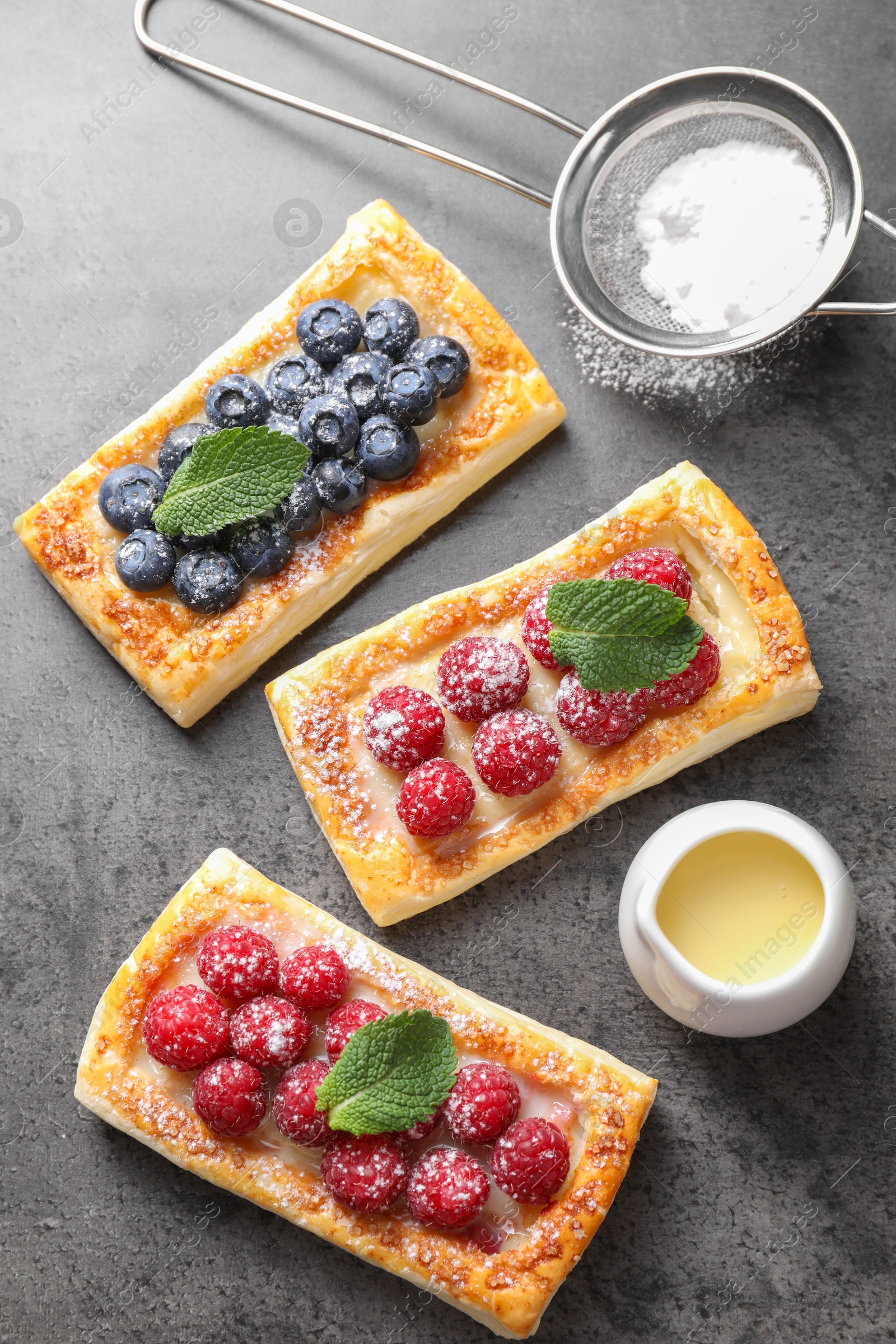 Photo of Tasty puff pastries with berries and powdered sugar on grey table, flat lay