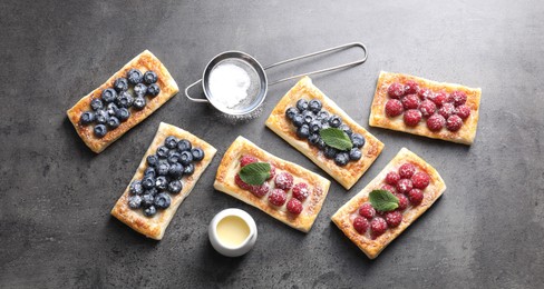 Tasty puff pastries with berries and powdered sugar on grey table, flat lay