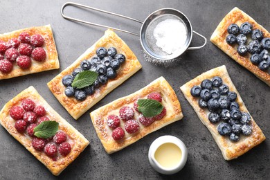 Tasty puff pastries with berries and powdered sugar on grey table, flat lay