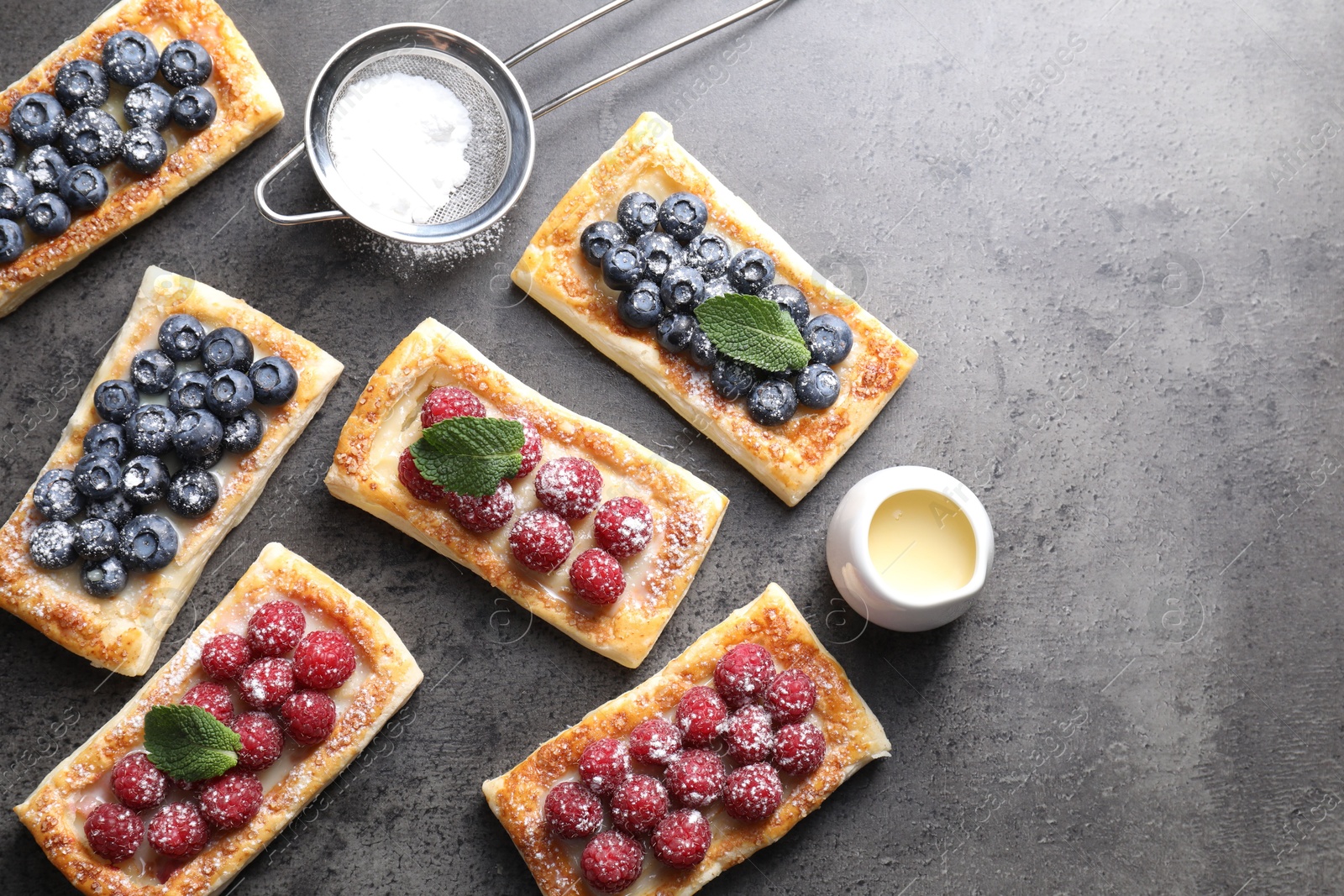 Photo of Tasty puff pastries with berries and powdered sugar on grey table, flat lay. Space for text