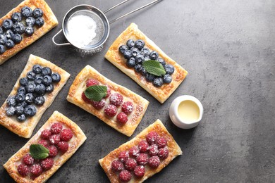 Tasty puff pastries with berries and powdered sugar on grey table, flat lay. Space for text