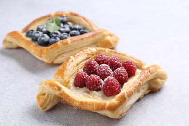 Tasty puff pastries with berries on white table, closeup