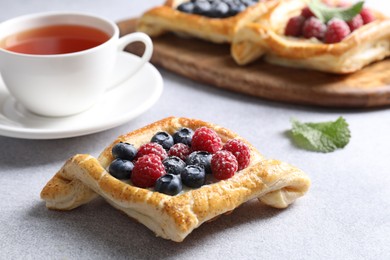 Photo of Tasty puff pastries with berries and tea on white table, closeup