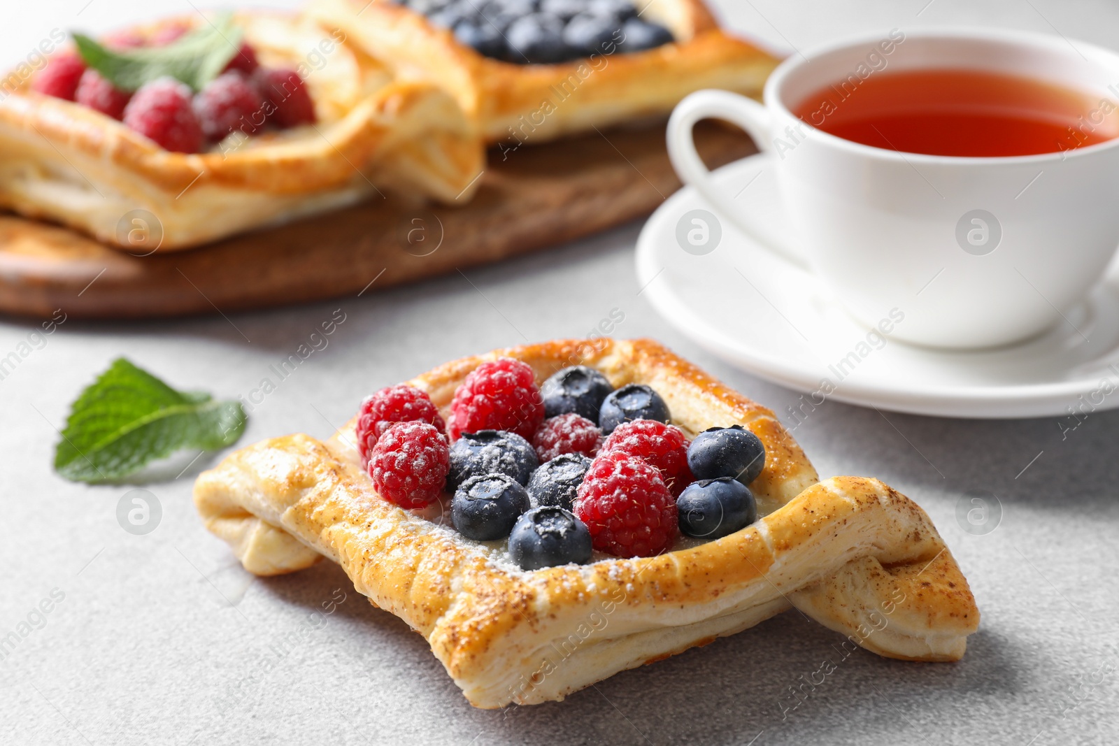 Photo of Tasty puff pastries with berries and tea on white table, closeup