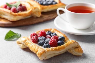 Photo of Tasty puff pastries with berries and tea on white table, closeup