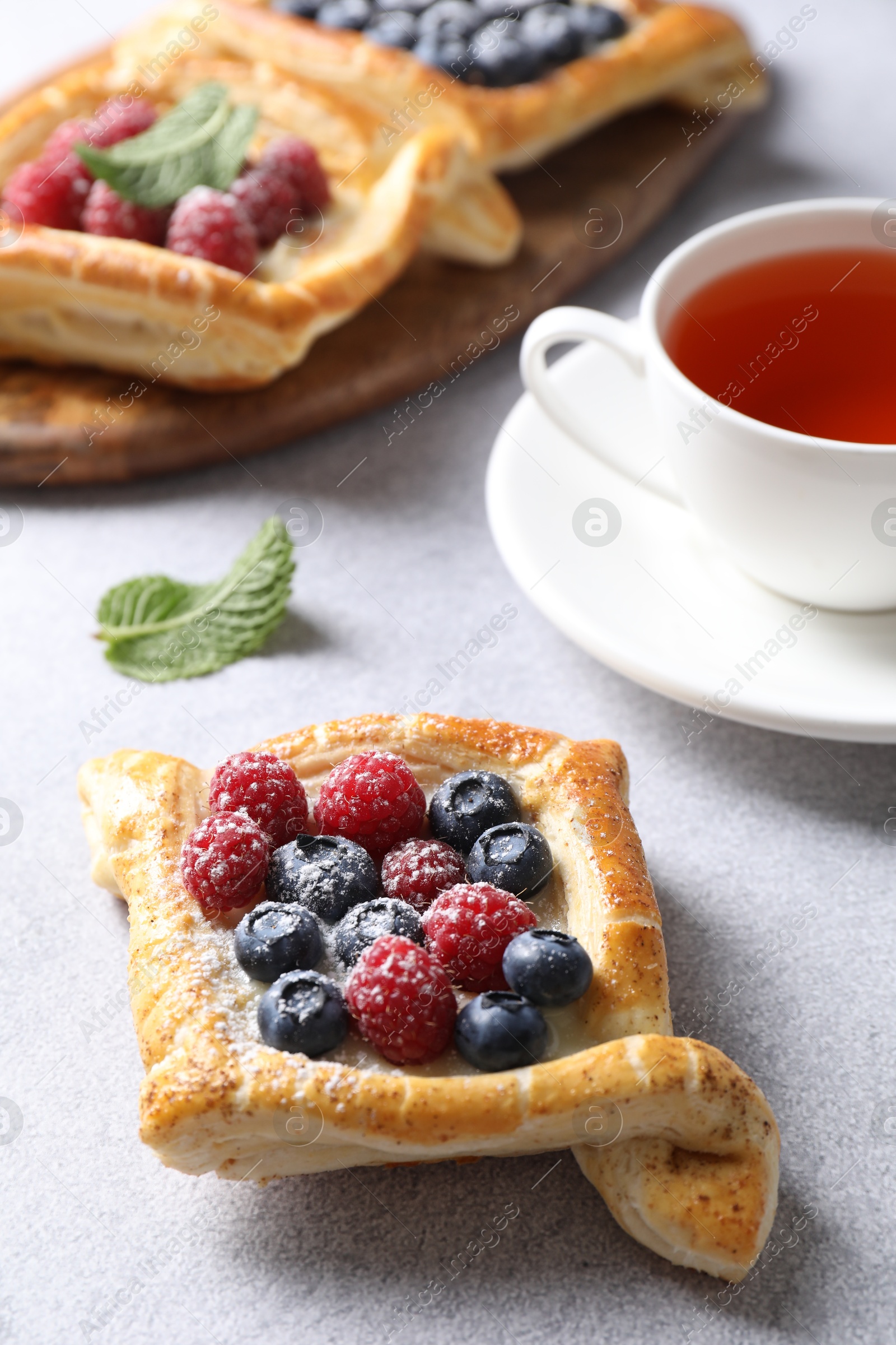 Photo of Tasty puff pastries with berries and tea on white table, closeup