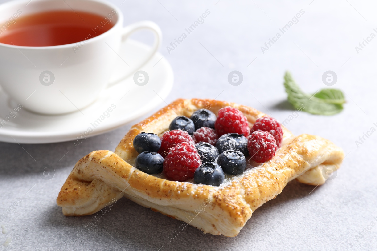 Photo of Tasty puff pastry with berries and tea on white table, closeup