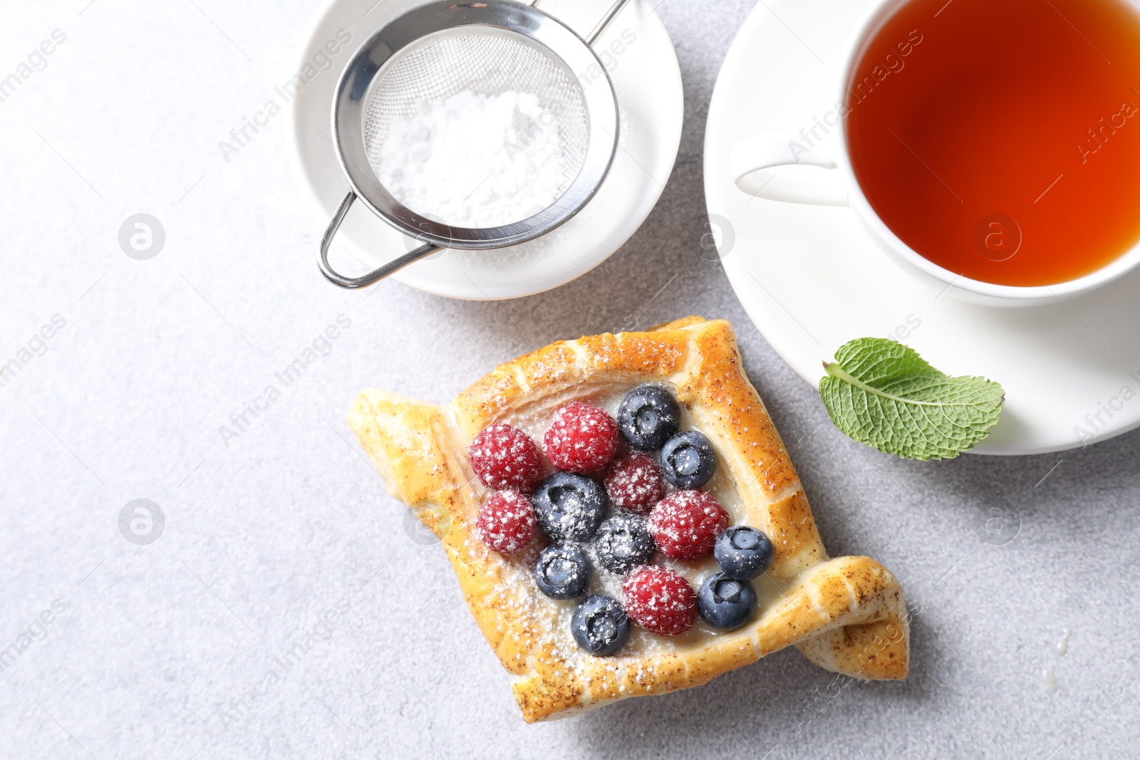 Photo of Tasty puff pastry with berries and tea on white table, flat lay. Space for text