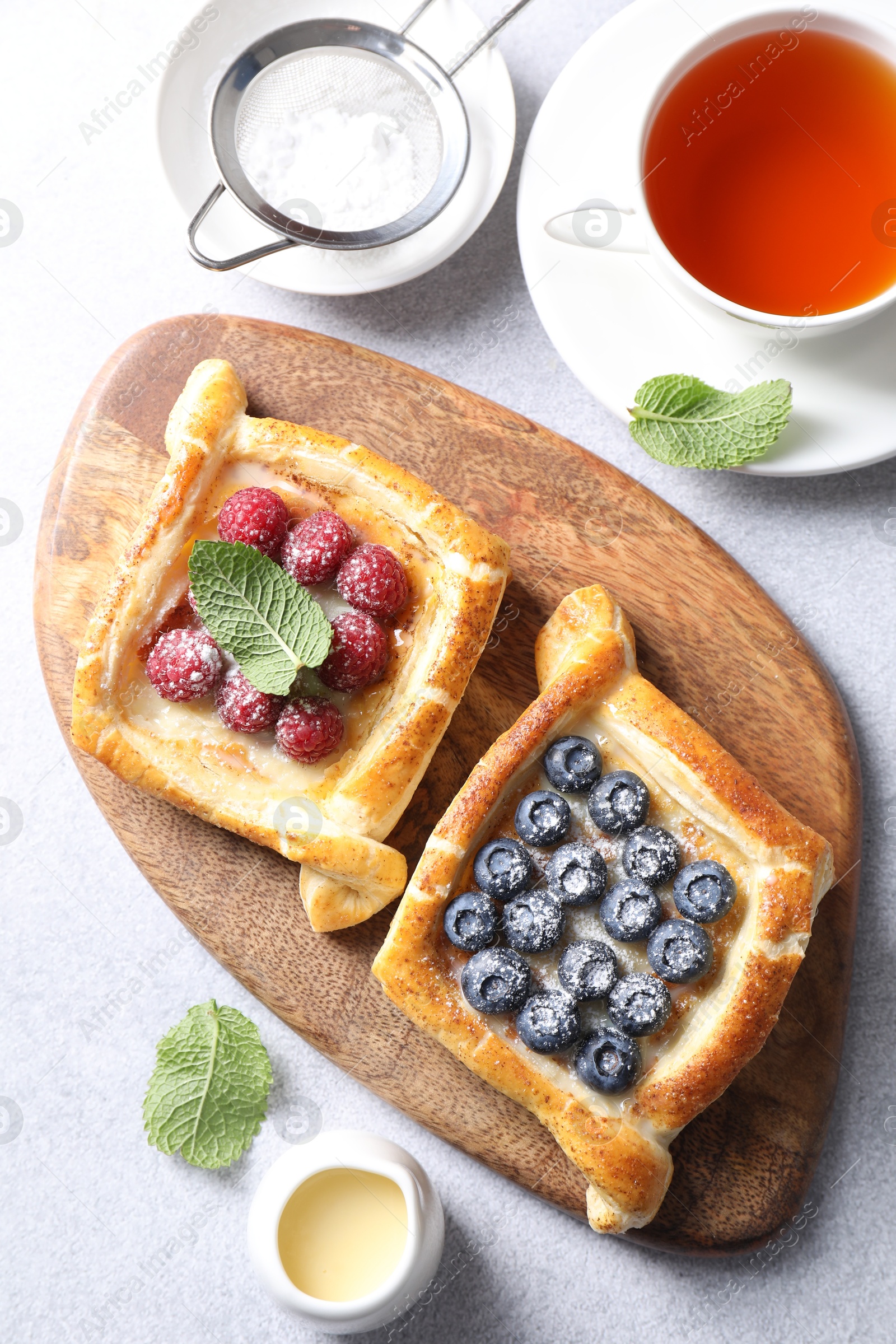 Photo of Tasty puff pastries with berries and tea on white table, flat lay