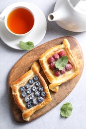 Tasty puff pastries with berries and tea on white table, flat lay