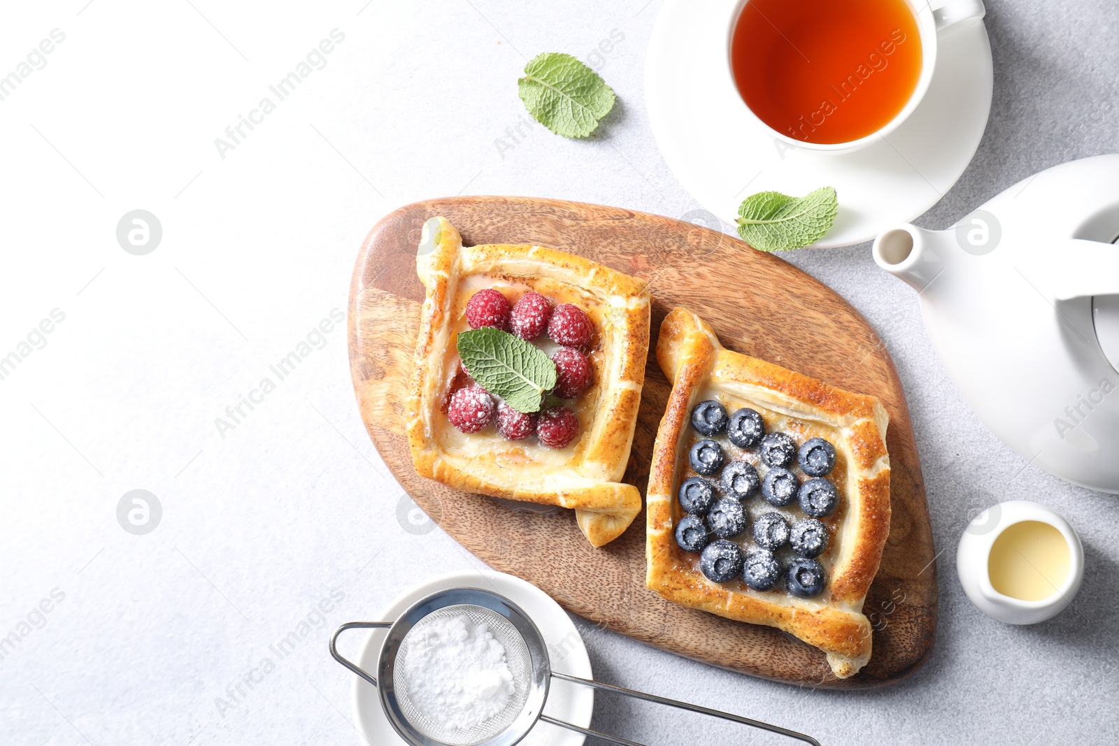 Photo of Tasty puff pastries with berries and tea on white table, flat lay. Space for text