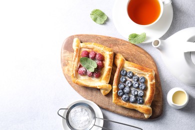 Photo of Tasty puff pastries with berries and tea on white table, flat lay. Space for text