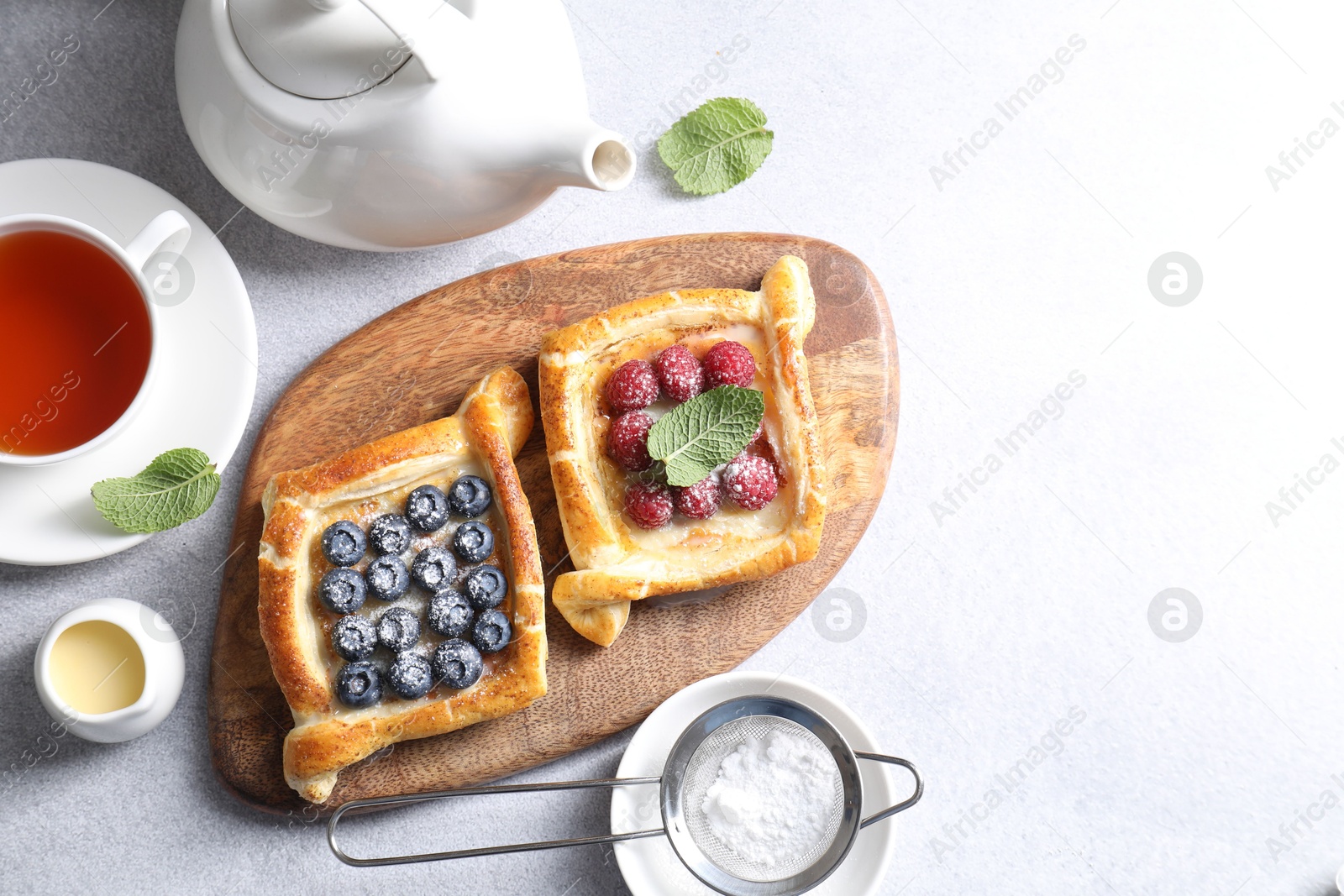 Photo of Tasty puff pastries with berries and tea on white table, flat lay. Space for text