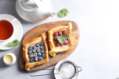 Photo of Tasty puff pastries with berries and tea on white table, flat lay. Space for text