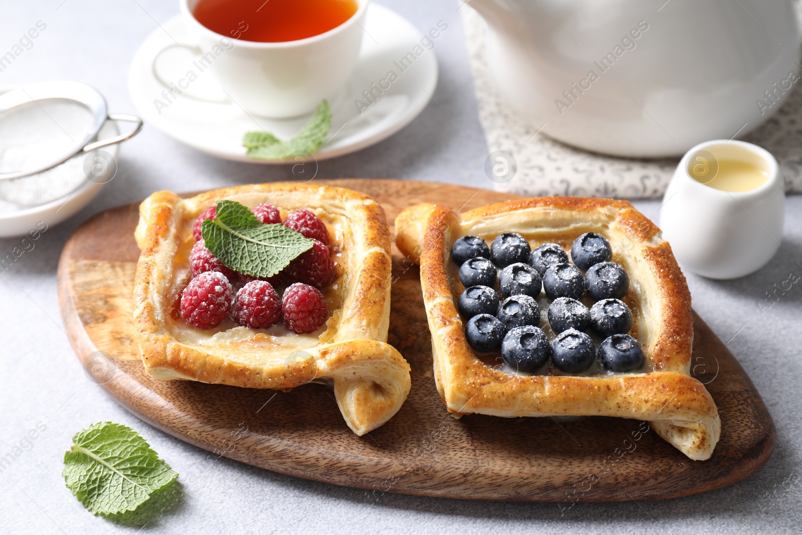 Photo of Tasty puff pastries with berries and tea on white table, closeup