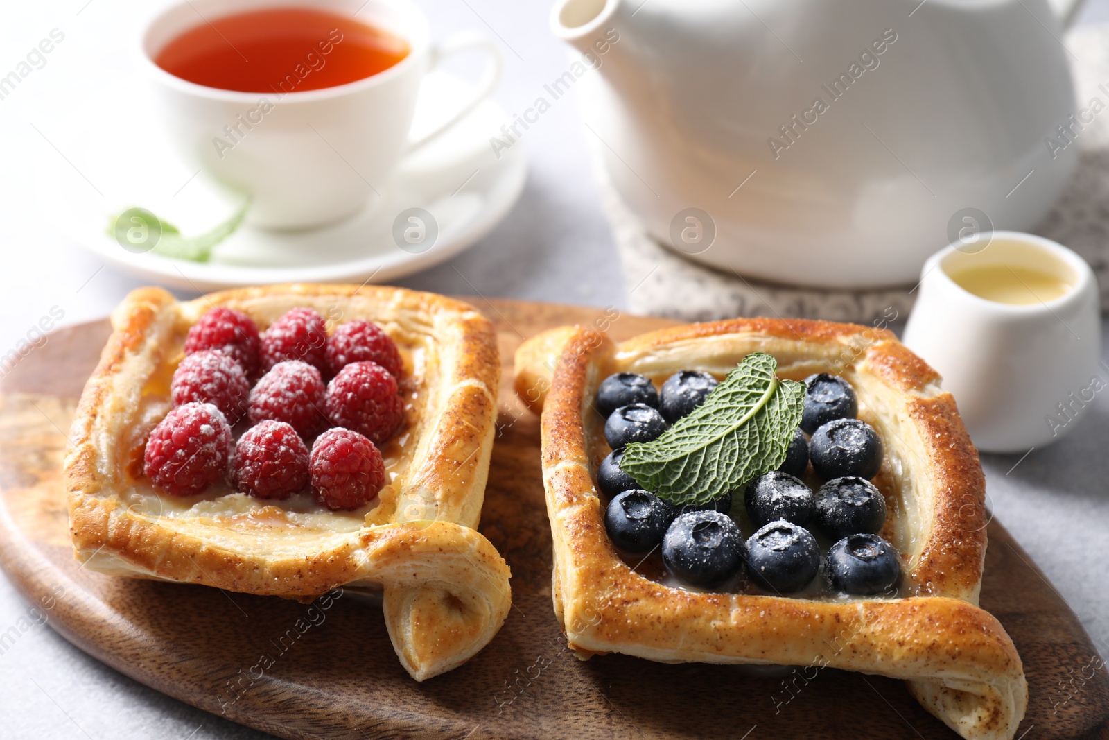 Photo of Tasty puff pastries with berries and tea on white table, closeup