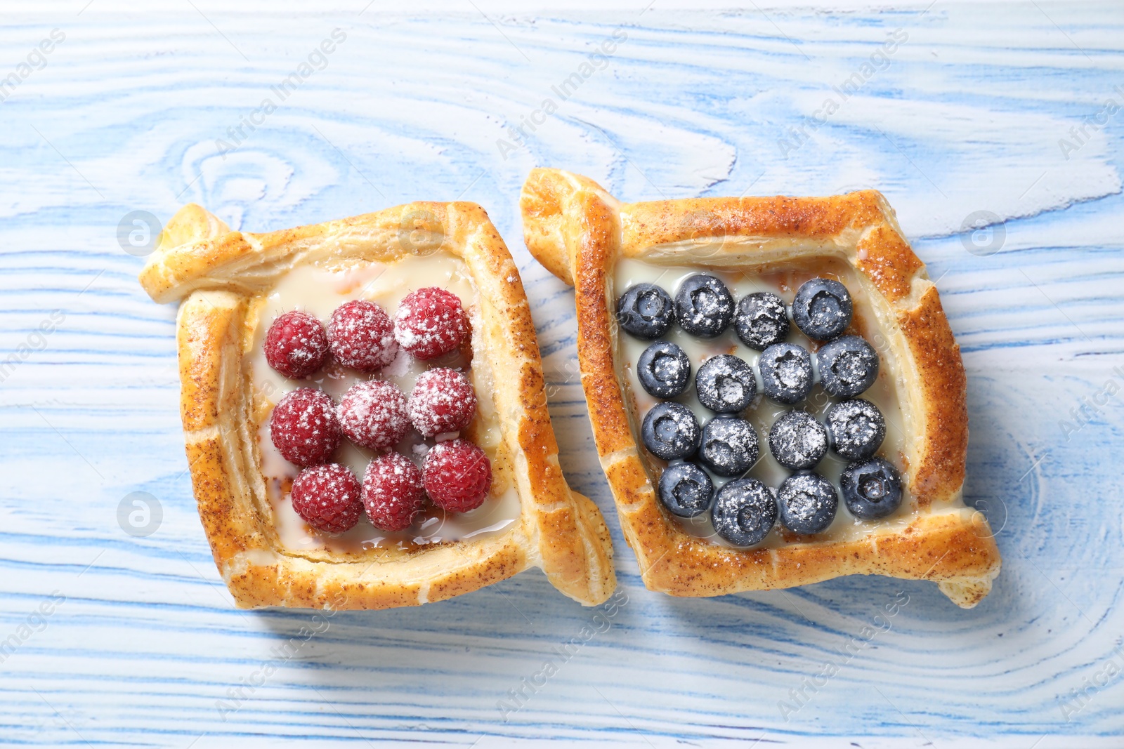 Photo of Tasty puff pastries with berries on light blue wooden table, top view