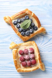 Tasty puff pastries with berries on light blue wooden table, top view