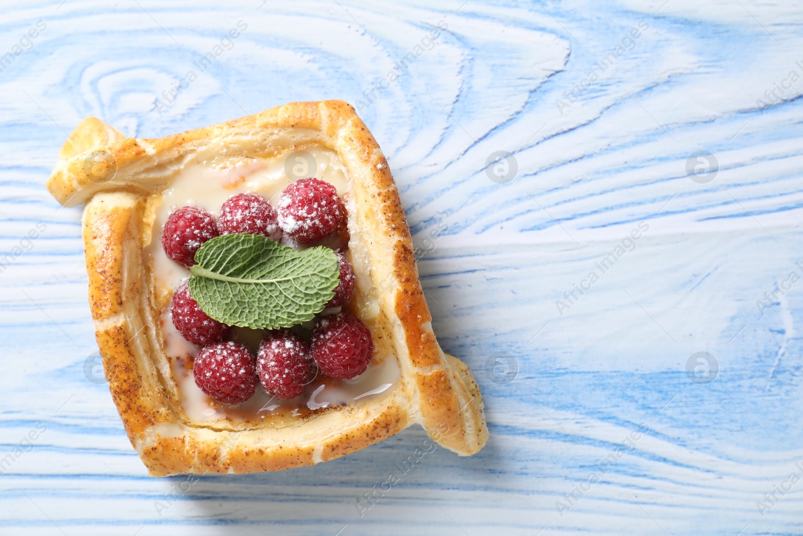 Photo of Tasty puff pastry with raspberries and mint on light blue wooden table, top view. Space for text