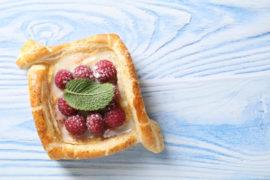 Tasty puff pastry with raspberries and mint on light blue wooden table, top view. Space for text