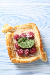 Tasty puff pastry with raspberries and mint on light blue wooden table, top view